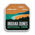 Indiana Dunes embroidered patch with orange sky, teal water, sandy shoreline, green landscape and white stitched border